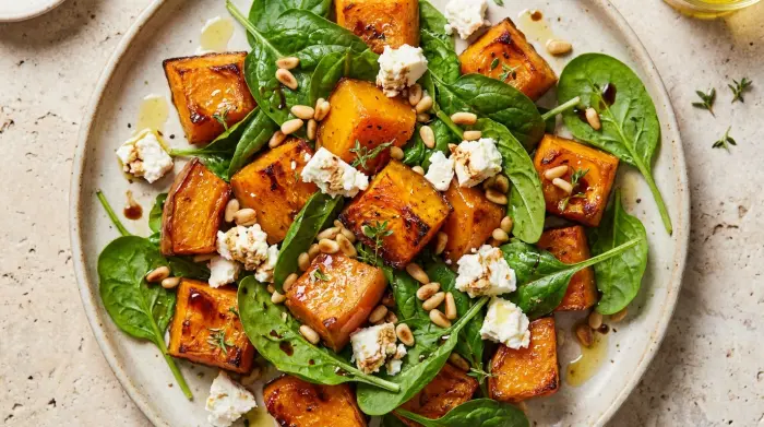 A colorful bowl of roast pumpkin, baby spinach, and feta salad ready to be served.
